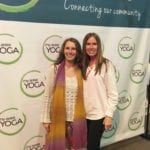 two women pose in front of a my area yoga banner