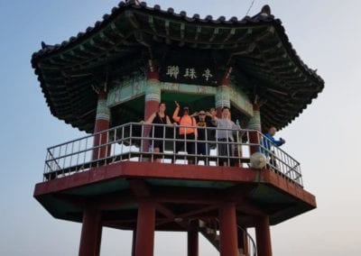 Group of people waving on top of a red and green Korean pavilion