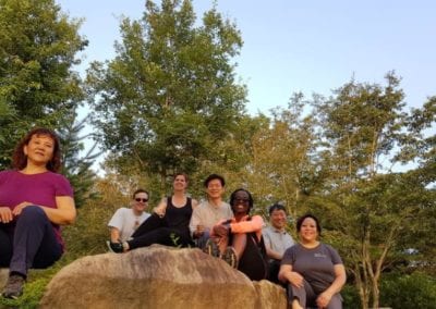 Group of people smiling while sitting on a large rock with trees in background