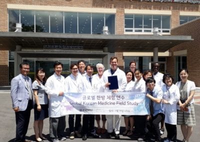 Large group of doctors and others holding "Global Korean Medicine Field Study" sign and one doctor holding a certificate