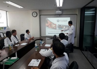 Doctor standing in front of screen presenting to small group of doctors