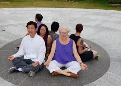 Six people sitting back-to-back in a meditating position in a circle on the ground.