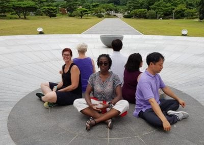 Six people sitting back-to-back meditating inside a circle on the ground.