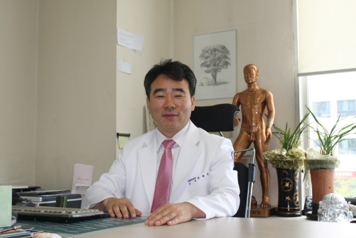 a man in a white coat and pink tie sits at a desk
