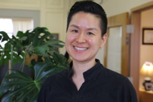 a woman in a black shirt smiles in front of a plant