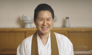 a woman wearing a white robe and a brown sash smiles for the camera