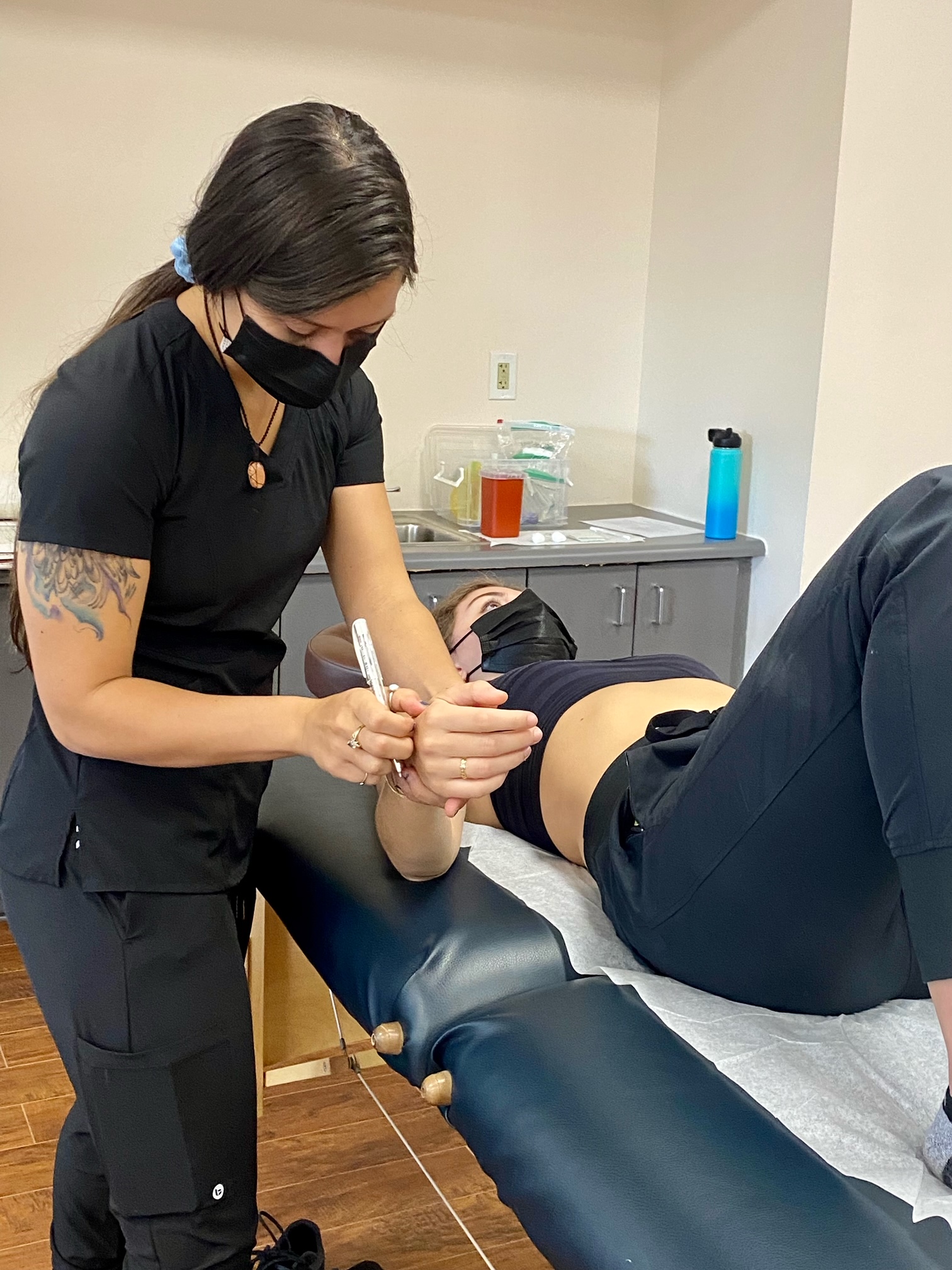 a woman wearing a mask is applying acupuncture to a womans arm