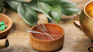 wooden bowl of acupuncture needles on a wooden table by plant.
